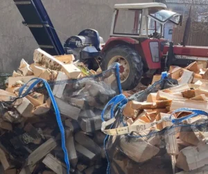 Zwei randvolle Bags mit Scheitholz vor einem roten Traktor