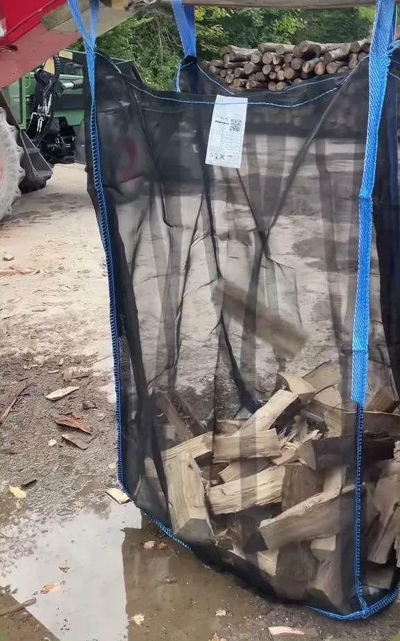 Big Bag wird am Lader befüllt, Holzstapel im Hintergrund